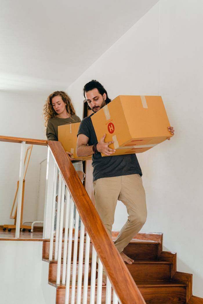services-01 Full body of young woman and barefoot ethnic man in casual clothes carrying boxes on wooden stairs while moving into new home