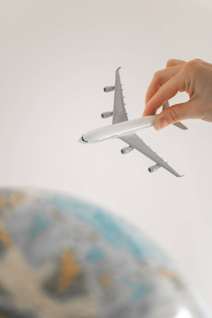 services-03 Close-up of a hand holding a toy airplane over a blurred globe, representing travel planning and adventure.